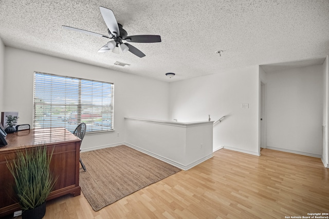 home office with ceiling fan, light hardwood / wood-style flooring, and a textured ceiling