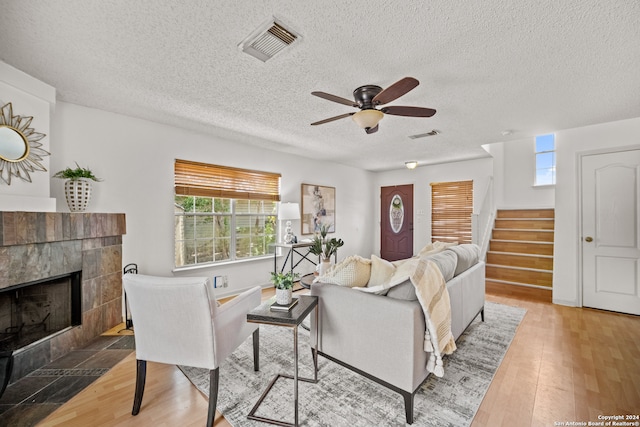 living room with a wealth of natural light, a tiled fireplace, and hardwood / wood-style flooring