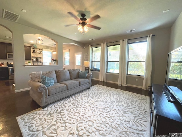 living room featuring arched walkways, visible vents, a textured ceiling, and baseboards