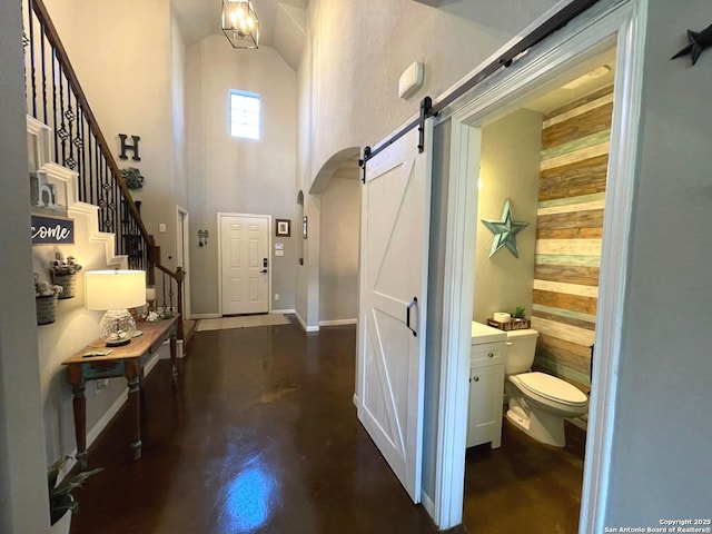 foyer entrance with arched walkways, concrete flooring, a barn door, a towering ceiling, and stairs