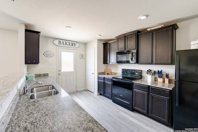 kitchen featuring dark brown cabinetry, light hardwood / wood-style floors, light stone counters, sink, and black appliances