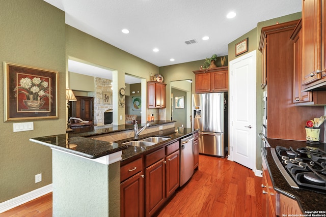 kitchen with dark stone counters, a stone fireplace, hardwood / wood-style floors, sink, and stainless steel appliances