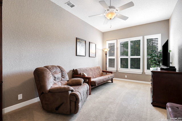 living area with a textured ceiling, ceiling fan, and light colored carpet