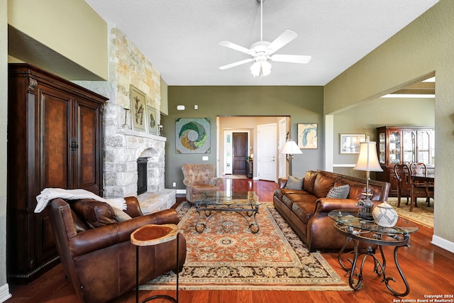 living room with hardwood / wood-style flooring, ceiling fan, a textured ceiling, and a stone fireplace