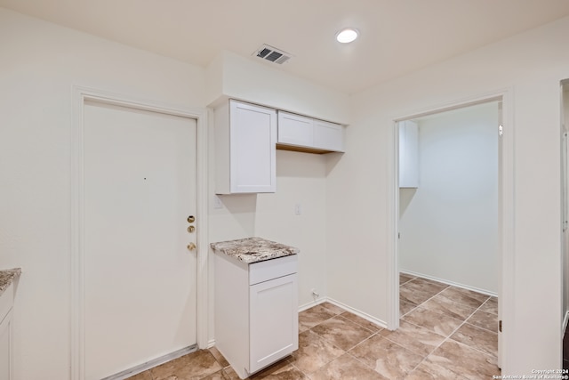 kitchen with light stone counters, white cabinetry, and light tile patterned floors