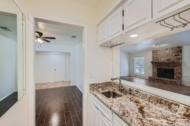 kitchen with ceiling fan, dark wood-type flooring, a brick fireplace, white cabinetry, and sink