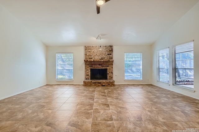 unfurnished living room featuring light tile patterned floors, brick wall, a brick fireplace, and a healthy amount of sunlight