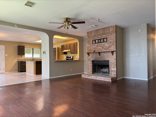 unfurnished living room with brick wall, a textured ceiling, ceiling fan, hardwood / wood-style flooring, and a brick fireplace