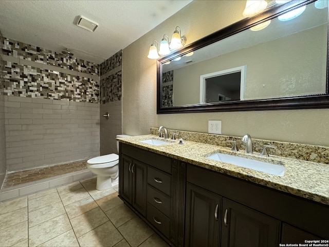 bathroom featuring toilet, tile patterned floors, tiled shower, dual bowl vanity, and a textured ceiling