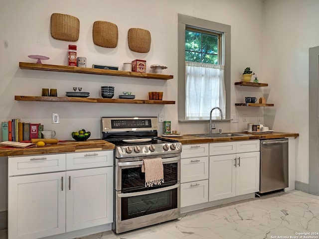 kitchen featuring sink, butcher block countertops, light tile patterned floors, stainless steel appliances, and white cabinets