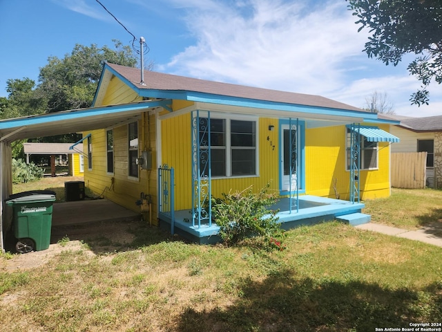 bungalow-style house with fence, central AC unit, a front lawn, and a carport