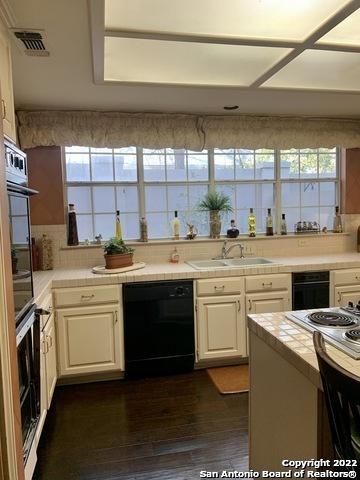 kitchen with dark hardwood / wood-style floors, tile counters, white cabinets, sink, and black dishwasher