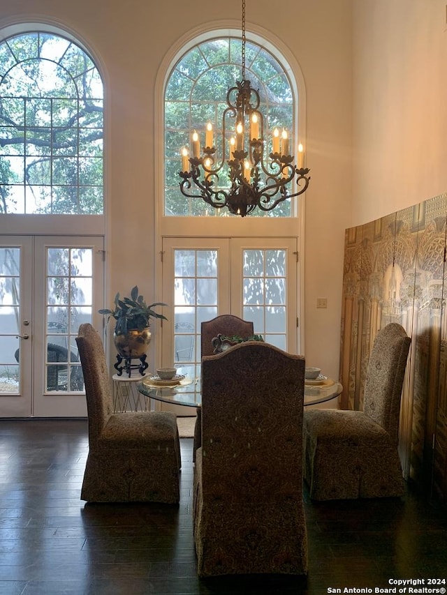 dining area featuring french doors, dark wood-type flooring, a towering ceiling, and a notable chandelier