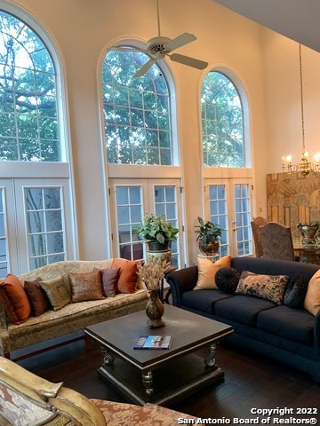 living room with a towering ceiling, french doors, ceiling fan with notable chandelier, and hardwood / wood-style floors