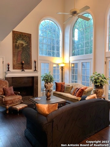 living room with hardwood / wood-style floors, a towering ceiling, ceiling fan, and a fireplace