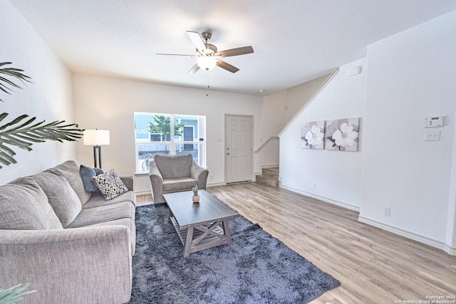 living area featuring baseboards, ceiling fan, stairway, and wood finished floors