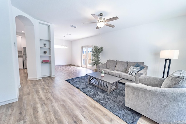 living room featuring light wood-style floors, arched walkways, baseboards, and ceiling fan with notable chandelier