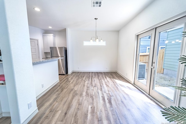 unfurnished dining area featuring a notable chandelier, visible vents, baseboards, french doors, and light wood-type flooring