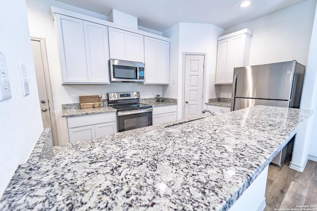 kitchen featuring light stone counters, appliances with stainless steel finishes, white cabinetry, a sink, and light wood-type flooring