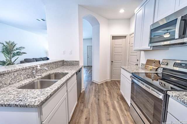 kitchen with arched walkways, a sink, white cabinets, appliances with stainless steel finishes, and light wood finished floors