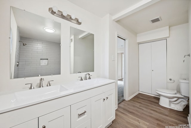 bathroom with a tile shower, toilet, hardwood / wood-style flooring, and vanity