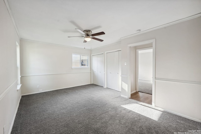 unfurnished bedroom featuring crown molding, multiple closets, ceiling fan, and carpet