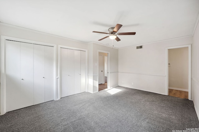 unfurnished bedroom with carpet flooring, two closets, ceiling fan, and crown molding