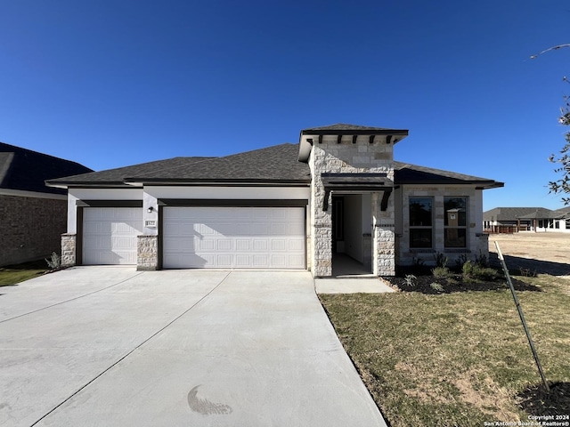 prairie-style home featuring a garage, stone siding, driveway, and a front lawn