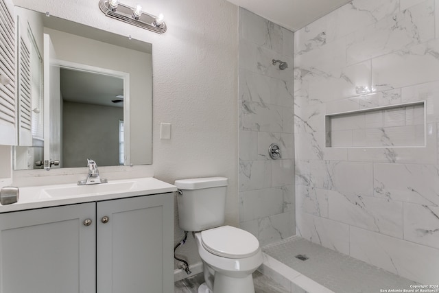 bathroom with toilet, a tile shower, and vanity