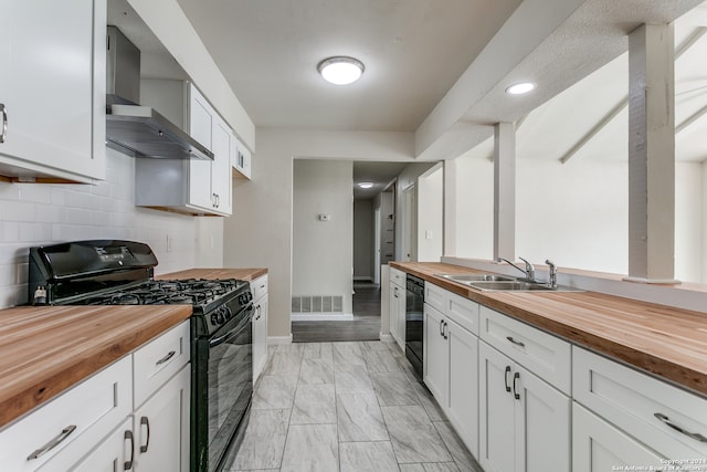 kitchen featuring wall chimney range hood, light hardwood / wood-style flooring, butcher block countertops, white cabinets, and black appliances