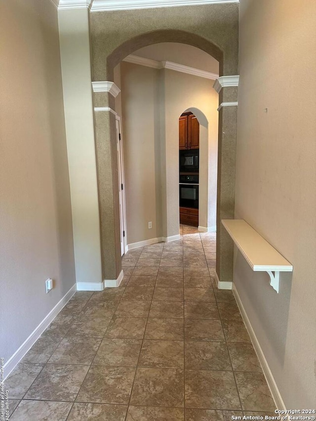 corridor with tile patterned floors, ornate columns, and ornamental molding