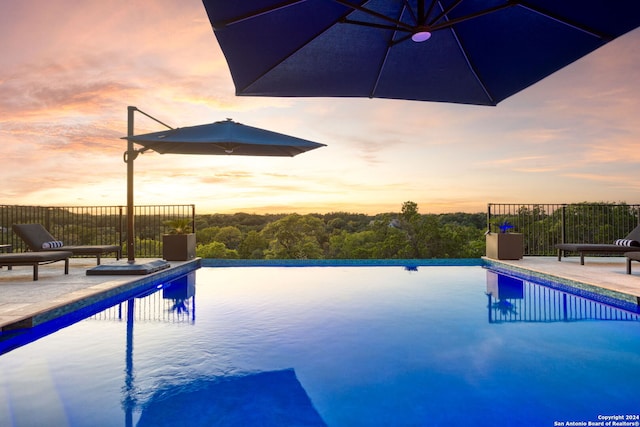 view of swimming pool featuring a patio area, an infinity pool, and fence