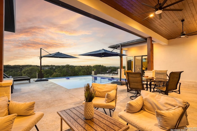 patio terrace at dusk featuring outdoor dining area, an outdoor hangout area, an infinity pool, and ceiling fan