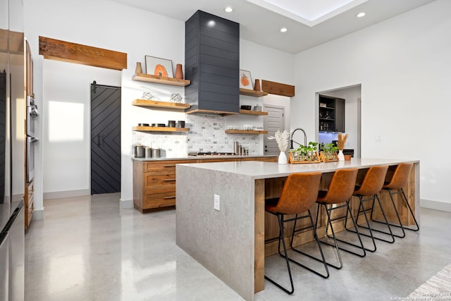 kitchen with a center island with sink, open shelves, tasteful backsplash, a barn door, and concrete flooring