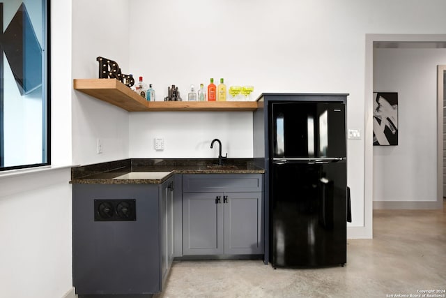 kitchen featuring gray cabinetry, open shelves, finished concrete floors, freestanding refrigerator, and a sink