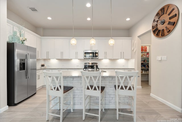 kitchen with backsplash, stainless steel appliances, light hardwood / wood-style floors, decorative light fixtures, and an island with sink