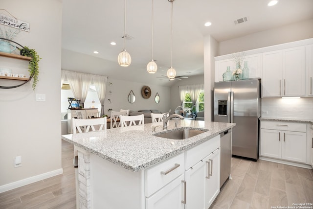 kitchen with ceiling fan, tasteful backsplash, a kitchen island with sink, white cabinetry, and sink