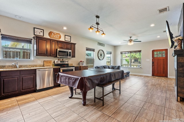 kitchen featuring hanging light fixtures, appliances with stainless steel finishes, light tile patterned floors, sink, and dark brown cabinets