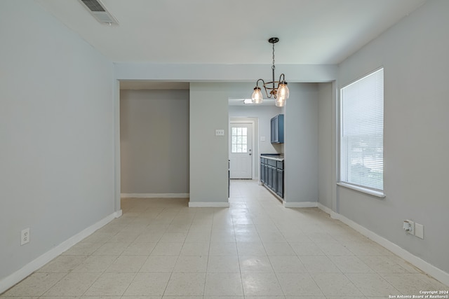 tiled spare room featuring an inviting chandelier