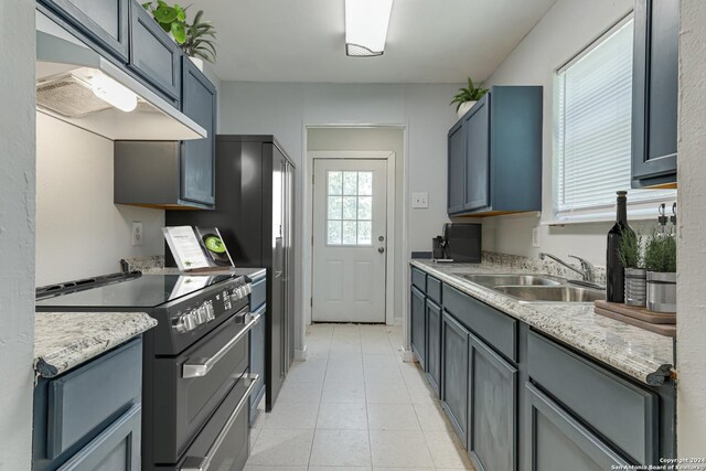 kitchen with range with two ovens, light tile patterned floors, under cabinet range hood, and a sink