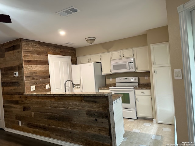 kitchen featuring sink, white appliances, wooden walls, light tile patterned floors, and white cabinets