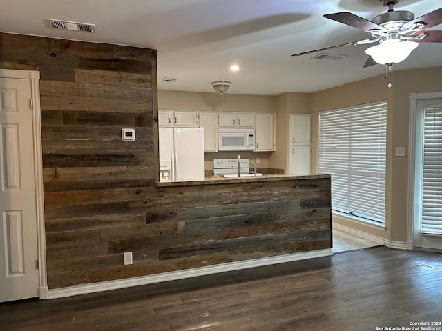 kitchen with white appliances, dark hardwood / wood-style floors, wooden walls, ceiling fan, and white cabinets