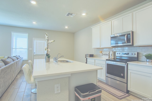 kitchen with backsplash, sink, appliances with stainless steel finishes, a kitchen island with sink, and white cabinets