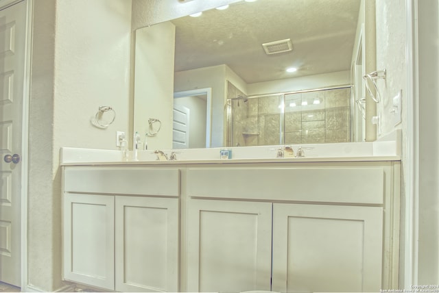 bathroom featuring a textured ceiling, double sink vanity, and a shower with door