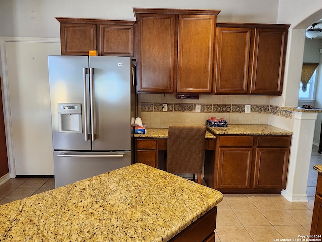 kitchen with decorative backsplash, light tile patterned flooring, stainless steel fridge, and light stone counters