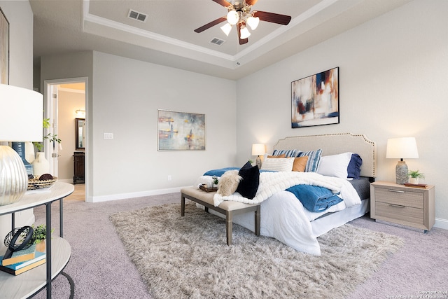 carpeted bedroom featuring a tray ceiling, ornamental molding, connected bathroom, and ceiling fan