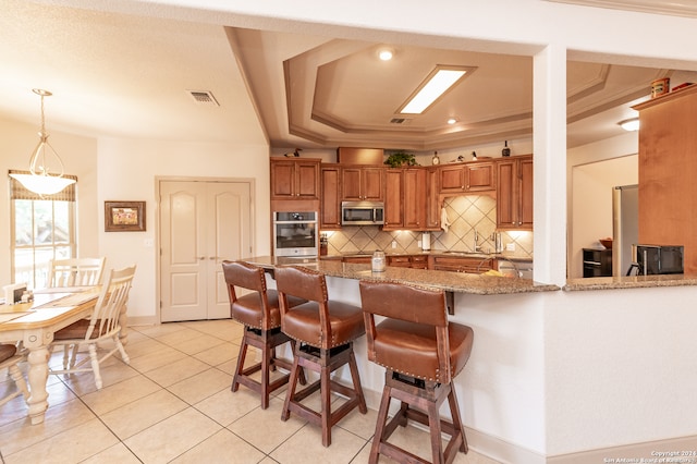 kitchen with appliances with stainless steel finishes, kitchen peninsula, tasteful backsplash, pendant lighting, and a tray ceiling