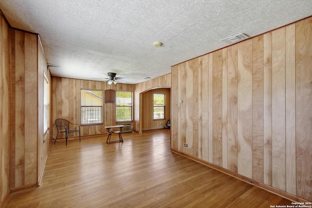 empty room featuring wood walls, ceiling fan, a textured ceiling, and hardwood / wood-style flooring