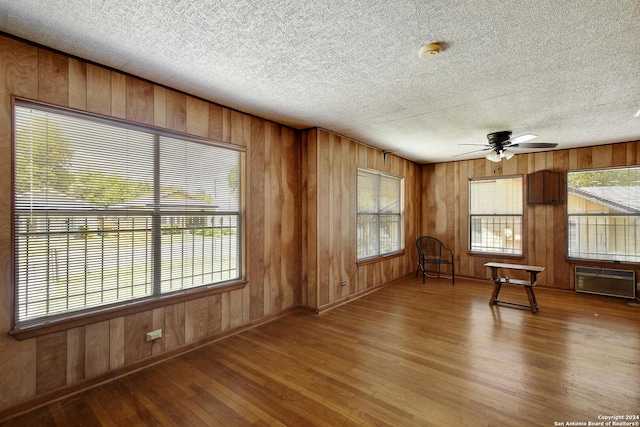 interior space with ceiling fan, wooden walls, hardwood / wood-style floors, and a textured ceiling