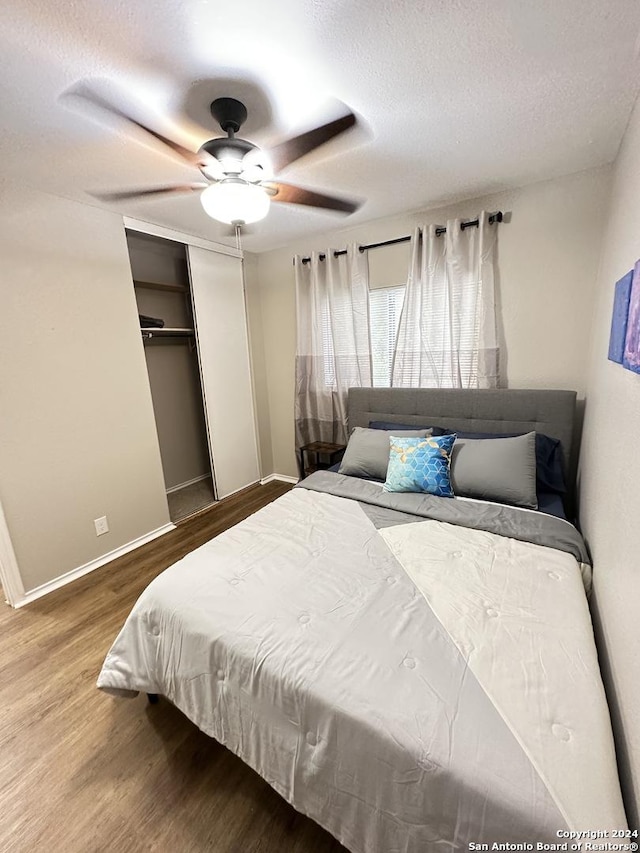 bedroom featuring baseboards, ceiling fan, wood finished floors, a textured ceiling, and a closet